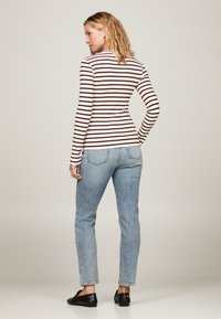 Camicia a maniche lunghe, aderente, con righe orizzontali bianche e bordeaux. Abbinata a jeans in denim azzurro chiaro, caratterizzati da un leggero effetto lavato e una vestibilità affusolata.