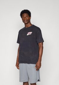 Čierne bavlnené tričko s krátkymi rukávmi, s ružovo-bielym logom Nike na hrudi. Oblečené s svetlošedými šortkami.