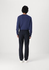Mørkeblå genser med rund hals, kombinert med svarte, elastiske joggebukser. Hvite joggesko fullfører antrekket. Glatt stofftekstur.