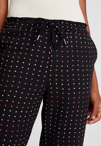 Pantalon noir à motifs avec une taille à cordon ; il comporte des pois rouges et blancs ; tissu lisse avec une coupe décontractée. Considéré comme un style casual.