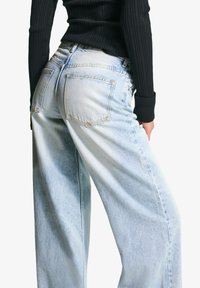 Svetlo modri kavbojki z ohlapnim krojem, z zadnjimi žepi in zbledelim videzom. Oblečeni z črnim rebrastim topom.