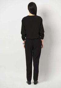 Schwarzes, locker sitzendes Outfit mit einem langärmeligen Oberteil und taillierten Hosen. Das Material scheint weich zu sein; die Bündchen und der Bund sind elastisch.