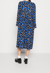 Abito nero con motivo astratto blu e bianco, dotato di maniche lunghe, un design a strati, indossato con scarpe platform nere e calzini bianchi.