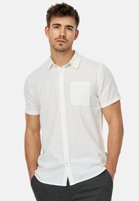 Camisa blanca de manga corta, hecha de tela ligera, con un cierre de botón en la parte delantera y un bolsillo en el pecho, con un corte relajado.