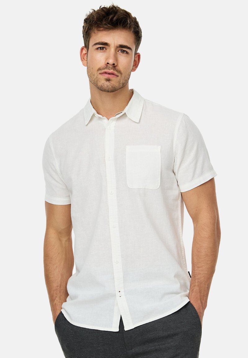 Camisa blanca de manga corta, hecha de tela ligera, con un cierre de botón en la parte delantera y un bolsillo en el pecho, con un corte relajado.