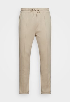 Pantalon de jogging beige ajusté avec taille élastique et cordon, avec des détails de coutures verticales et des chevilles resserrées.