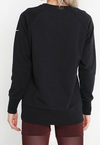 Sweatshirt noir avec des manches raglan, poignets et ourlet côtelés, texture douce. Présente un petit logo sur l'épaule.