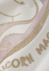 Weißer Stoff mit einem rosa und glitzernden goldenen Akzent, der ein Einhorn-Design und den Text "EINZIGARTIGE MAGIE" in erhabenen glitzernden goldenen Buchstaben zeigt.