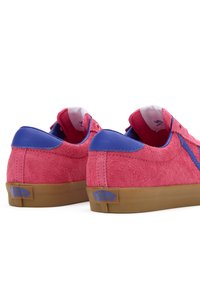Pink suede sneakers with blue leather accents, featuring a rubber gum sole and logo detail on the heel. Low-top design with textured finish.