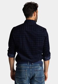 Donkerblauwe geruite shirt met opgerolde mouwen, gemaakt van een zachte stof, gedragen over blauwe denim jeans met gedetailleerde achterzakken.