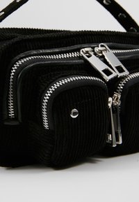 Sac en tissu noir texturé avec plusieurs fermetures éclair argentées et petites poches avant sur fond blanc.