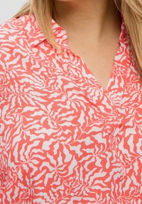 Czerwona i biała bluzka w wzory z dyskretnym wzorem fal, z kołnierzykiem i lekkim, teksturowanym materiałem.