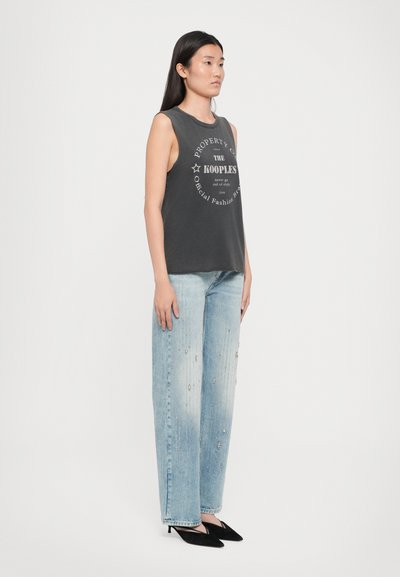 Grå ermeløs topp med trykt logo-design, akkompagnert av lyseblå vide jeans med utsmykninger og svarte spisse hæler.