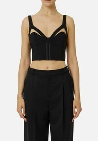 Top noir court avec des bretelles découpées, un corsage structuré et un détail de couture verticale. Associé à un pantalon noir taille haute.