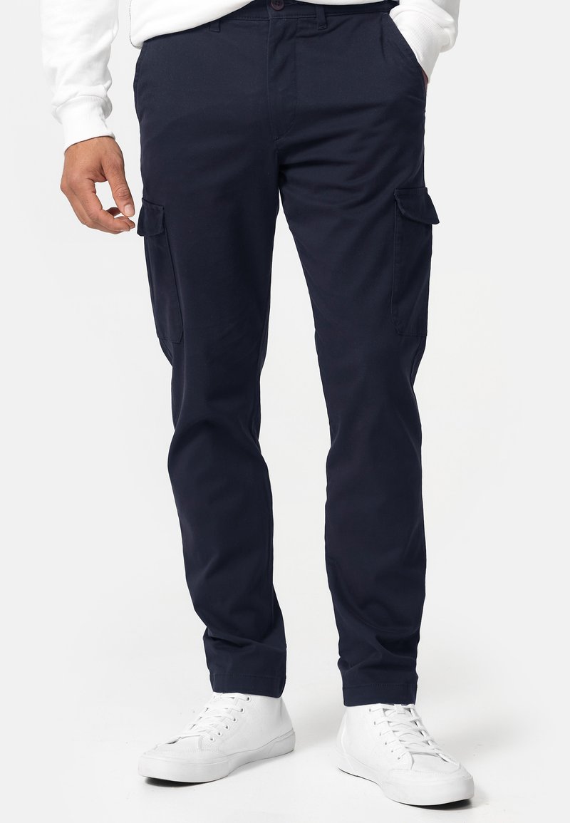 Pantalones cargo de la marina hechos de una mezcla de algodón, con bolsillos laterales, un corte recto y un acabado liso y texturizado. Combinados con zapatillas blancas.