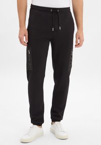 Zwarte joggerbroeken met elastische tailleband, ritszakken aan de zijkanten, ribgebreide boorden, gemaakt van zachte stof, gecombineerd met witte sneakers.