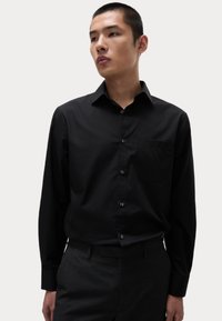 Zwart langarm overhemd met een down collar, enkele borstzak, gladde textuur en een regular fit. Gecombineerd met donkere broeken.