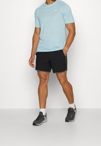 Camisa atlética de manga corta azul claro con una textura sutil, combinada con pantalones cortos negros con acentos grises. Llevada con zapatos deportivos negros.