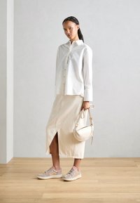 Camisa branca de botões, saia midi bege com fenda, ténis rosa claro e uma pequena mala creme. Tecido suave, linhas limpas, design minimalista.
