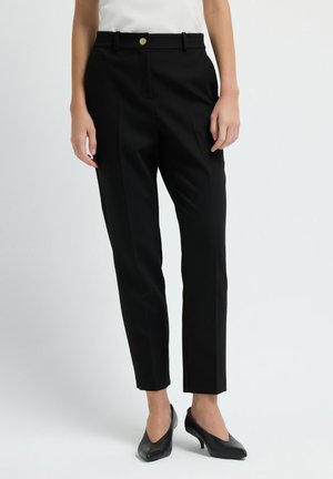 Black tailored trousers with a slim fit, featuring a gold button closure, belt loops, and a smooth texture. Worn with black pointed heels.