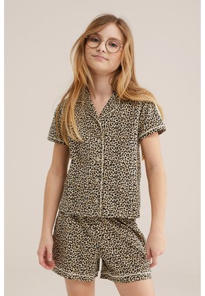Hosszú szőke hajú, kerek szemüveges lány, aki passzoló rövid ujjú, leopárdmintás gombos inget és rövidnadrágos pizsamát visel.