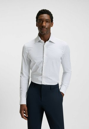 Camicia bianca con motivo a pois blu, maniche lunghe, colletto standard, abbinata a pantaloni blu navy. Tessuto di trama liscia.