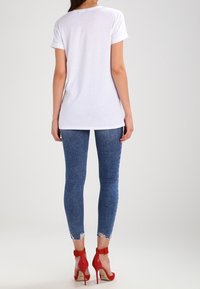 Vit bomull t-shirt med uppvikta ärmar, i kombination med blå slim fit-jeans med slitna fållar och röda hälskor med ankelremmar.