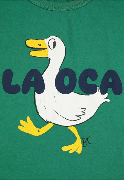 Zelené tričko s bielym kresleným kačicom so žltým zobákom a nohami, doplnené textom "LA OCA" tučnými námorníckymi písmenami.