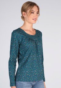 Langärmliges türkisfarbenes Oberteil mit floralem Muster in Grün und Rot, mit Rundhalsausschnitt und leichtem Plissierung am Brustbereich.