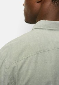 Hellgrünes Hemd aus strukturiertem Stoff mit einem dezenten Muster, Kragen und sichtbaren Nahtdetails auf der Rückseite.