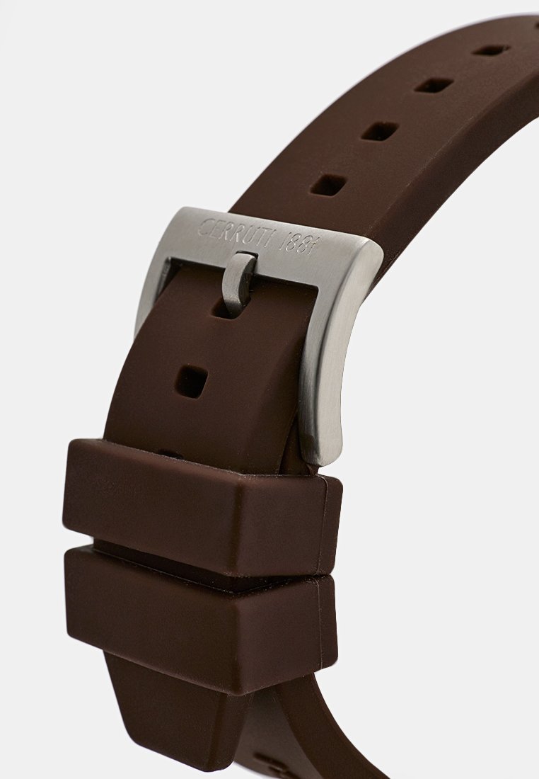 Bracelet de montre en caoutchouc brun avec boucle en métal argenté, présentant des accents rectangulaires et plusieurs trous pour l'ajustabilité. Marqué "CERRUTI 1881".