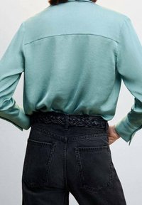 Turkis satin-skjorte med lange ærmer, der har en flad krave og en glat tekstur, sammen med høj talje sorte denim jeans med et fletbælte.