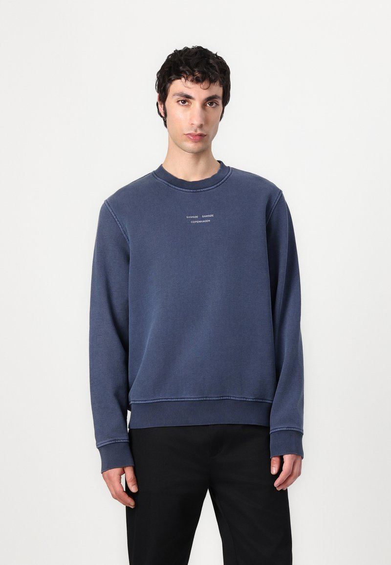 Felpa girocollo blu navy con polsini e orlo a coste, caratterizzata da un piccolo logo bianco sul petto, realizzata in tessuto morbido.