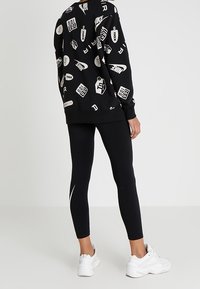 Svart sweatshirt med vita logotyper, matchad med svarta leggings med ett vitt accentband och vita sneakers.