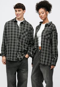 Fekete és szürke kockás gombos ingek elülső zsebekkel, fehér és szürke felsők fölött viselve, sötét farmernadrággal párosítva. Sima anyagtextúra.