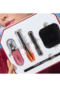Set de maquillaje KIKO que incluye un brillo labial rosa, máscara de pestañas, lápiz de cejas y un compacto en una bandeja blanca con una caja roja y acentos de logotipo.