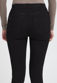 Černé džíny s vysokým pasem a hladkou texturou, s dekorativním prošíváním, dvěma zadními kapsami a štíhlým střihem.