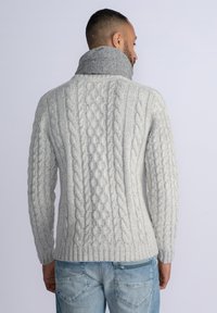 Suéter gris de punto trenzado con un cuello gris enrollado, que presenta patrones texturizados y un dobladillo acanalado, combinado con jeans de color azul claro.