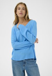 Haut à manches longues bleu clair en tissu texturé avec un décolleté en V, associé à un jean en denim bleu, caractérisé par une coupe décontractée et une chute souple.