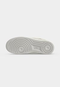 Σόλα λευκού αθλητικού παπουτσιού Nike με κυκλικά σχέδια πέλματος και λογότυπο Nike που είναι σκαλισμένο κοντά στη μέση, σε απλό φόντο.