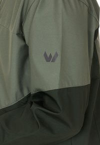 Green waterproof jacket featuring a two-tone design with a smooth texture. Includes a dark logo on the left sleeve.