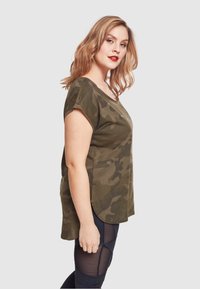 Oliven grønn camo topp med korte ermer, avslappet passform, rund hem og myk tekstur. Kombinert med sorte leggings med meshdetaljer.