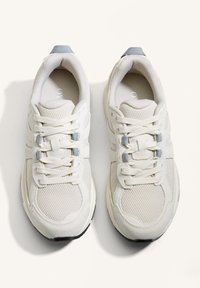 Vita träningsskor i mesh och mockamaterial. Har snörning, ljusblå accenter och en strukturerad sula.