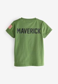 Zelené bavlněné tričko s nápisem "MAVERICK" v tučném černém písmu na zádech, s nášivkou americké vlajky na levém rukávu.