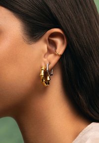 Orecchini a cerchio in oro e argento con un design simile al bambù, caratterizzati da texture lucide e forme diverse, mostrati su uno sfondo di tonalità naturali.