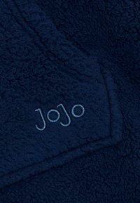 Granatowy polarowy materiał z teksturowaną powierzchnią. Zawiera wyszywane logo "JoJo" w jasnoniebieskiej nici, umieszczone w pobliżu szwu.