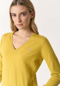 Pullover giallo a scollo a V realizzato in morbido tessuto con collo a coste. Presenta un piccolo logo ricamato sul petto sinistro.