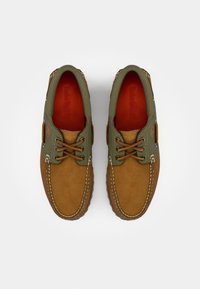 Braune Wildlederschuhe mit grünen Lederakzenten, Schnürverschluss, kontrastierenden Nähten und orangen Einlegesohlen. Sie haben eine runde Zehenform und ein strukturiertes Material.
