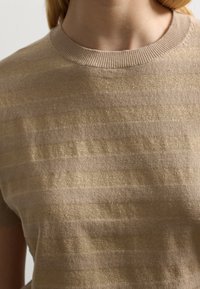 Beige gebreid sweater met korte mouwen, met een textuurdesign dat is gemaakt door afwisselend matte en glanzende gouden strepen. Geribbelde halslijn.