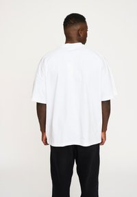 Hvid oversized T-shirt med korte ærmer og rund halsudskæring, lavet af et glat bomuldsstof. Har en lige kant og afslappet pasform.